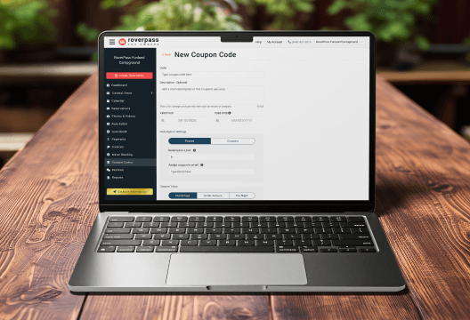 Laptop on a wooden table showing the RoverPass dashboard with the New Coupon Code form for creating promo codes