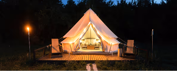 Illuminated luxury bell tent on a wooden deck at night, surrounded by nature and warm ambient lighting.