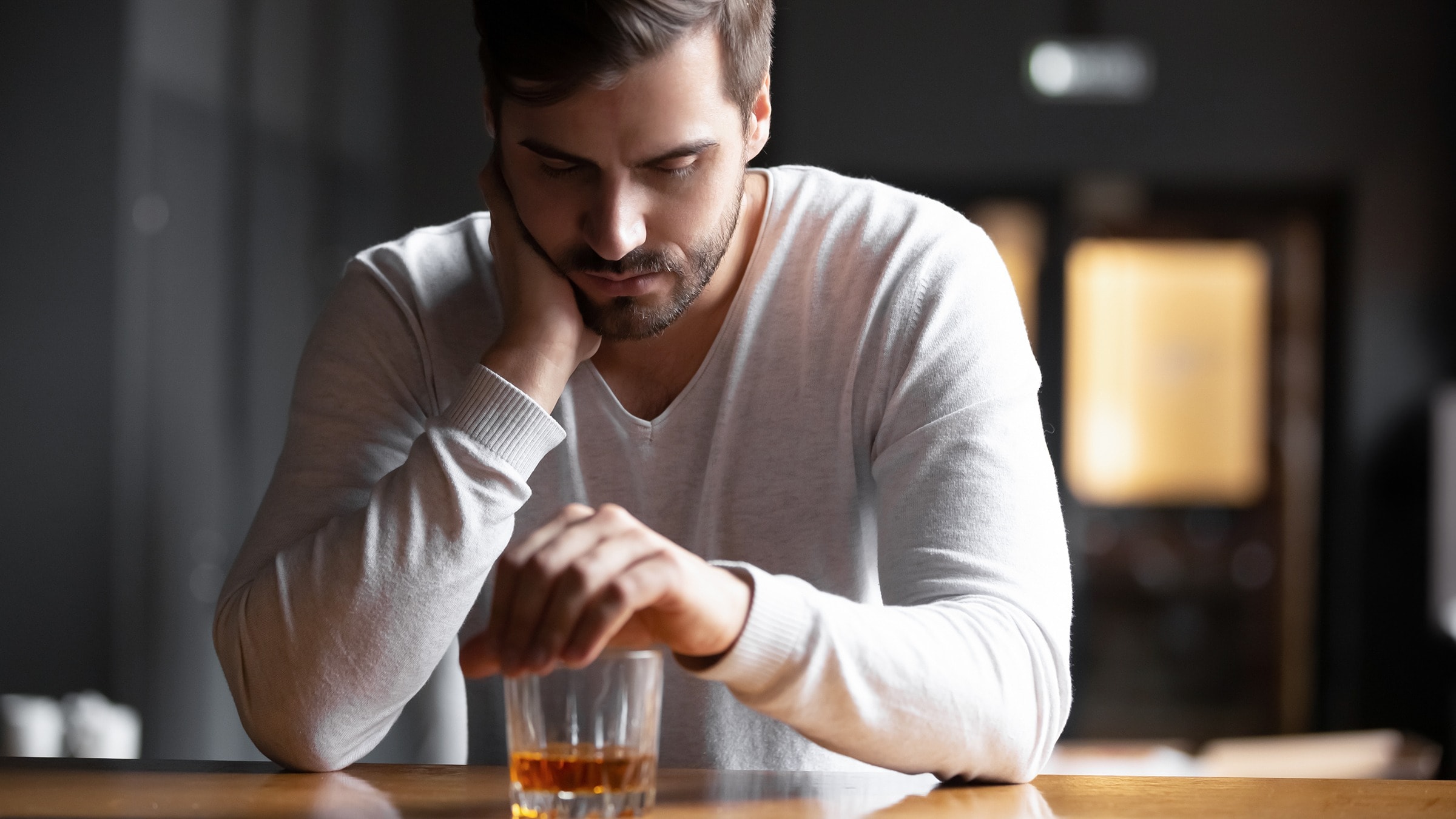 A person looking contemplative while holding a glass of alcohol, pondering if it is safe to drink alcohol while on Suboxone.