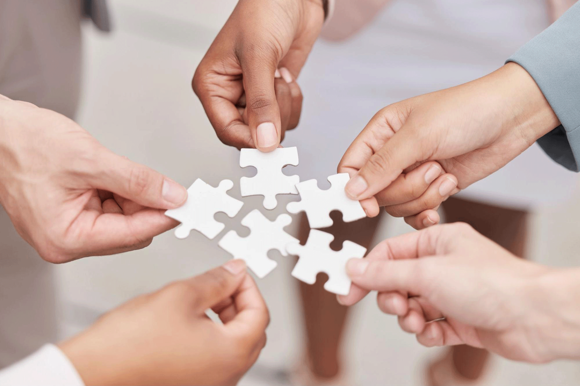 Close-up of diverse hands connecting puzzle pieces, symbolising inclusive communication, psychological safety, and building team trust through collaboration in the workplace