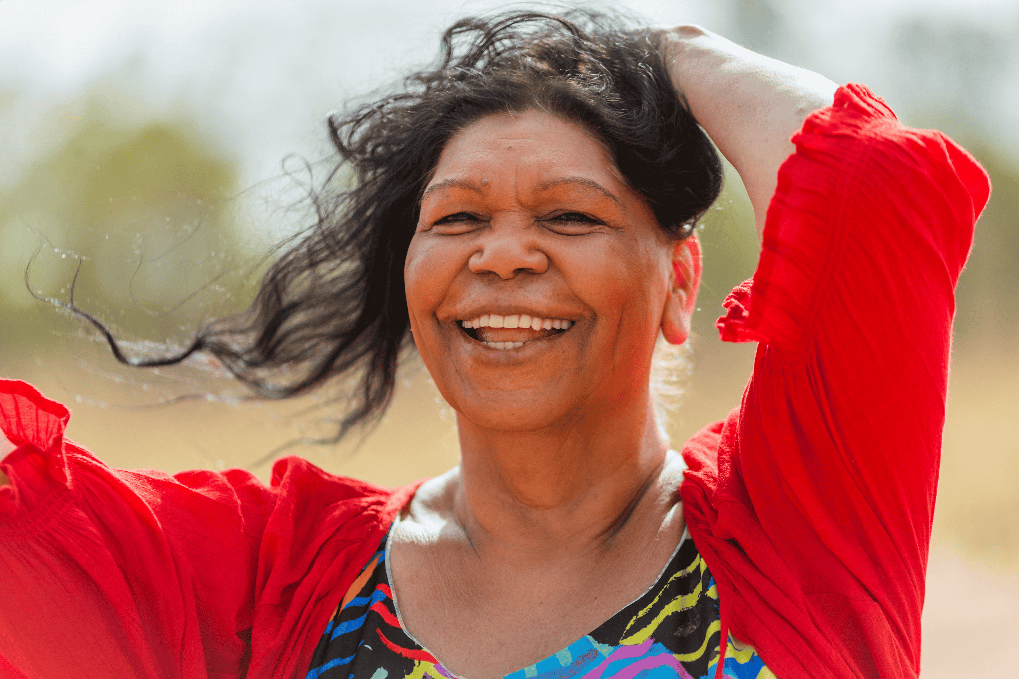 Smiling woman with long black hair wearing a blue floral-patterned blouse against a black background.