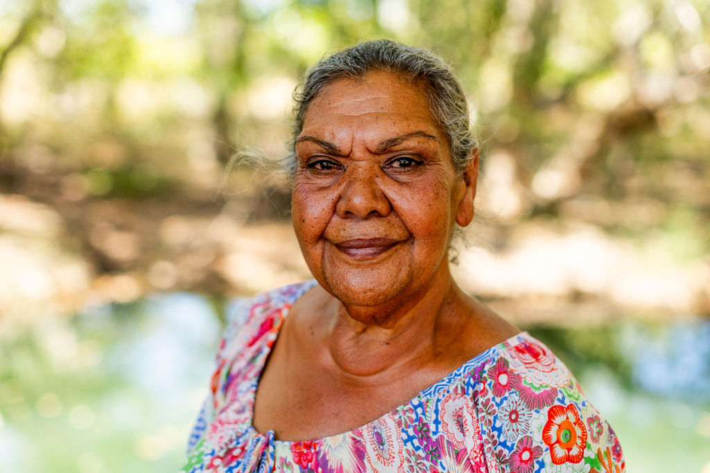 Portrait of an older woman outdoors wearing a colorful floral blouse with a calm expression.