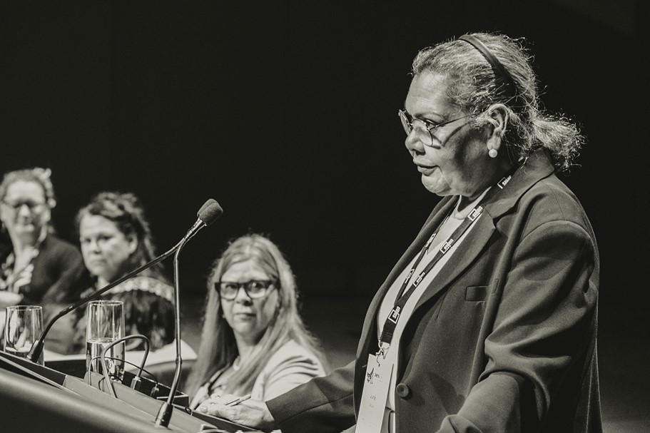 June Oscar standing at lectern, looking at crowd.