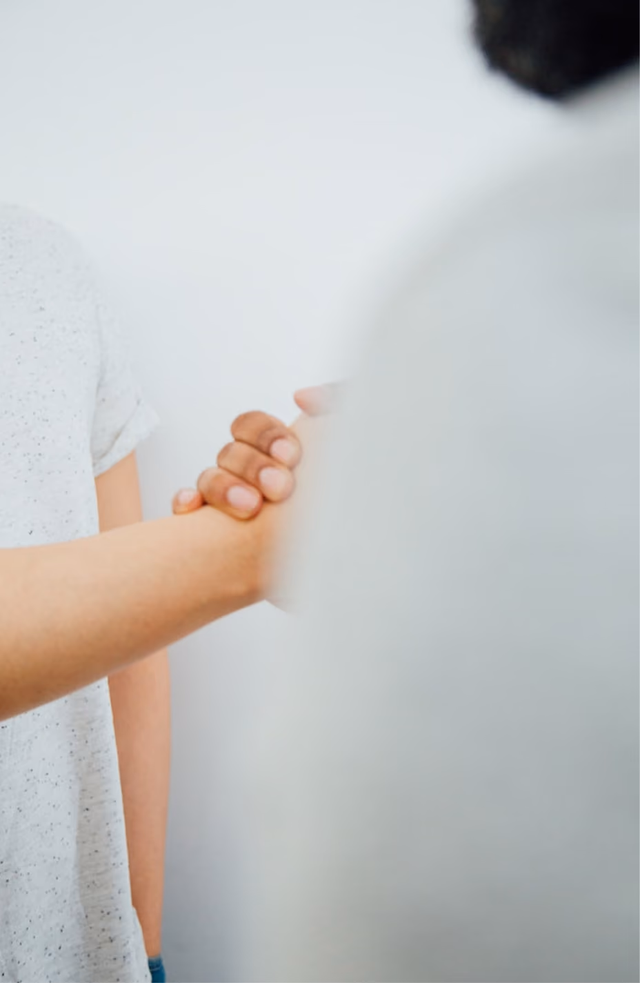 Two people shaking hands, one wearing a white speckled shirt, against a plain light background.