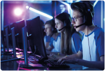 Team of young esports players wearing headsets, sitting in a row at computer monitors under neon lighting, fully focused on gameplay in a competitive gaming environment. No in-game advertising is visible.
