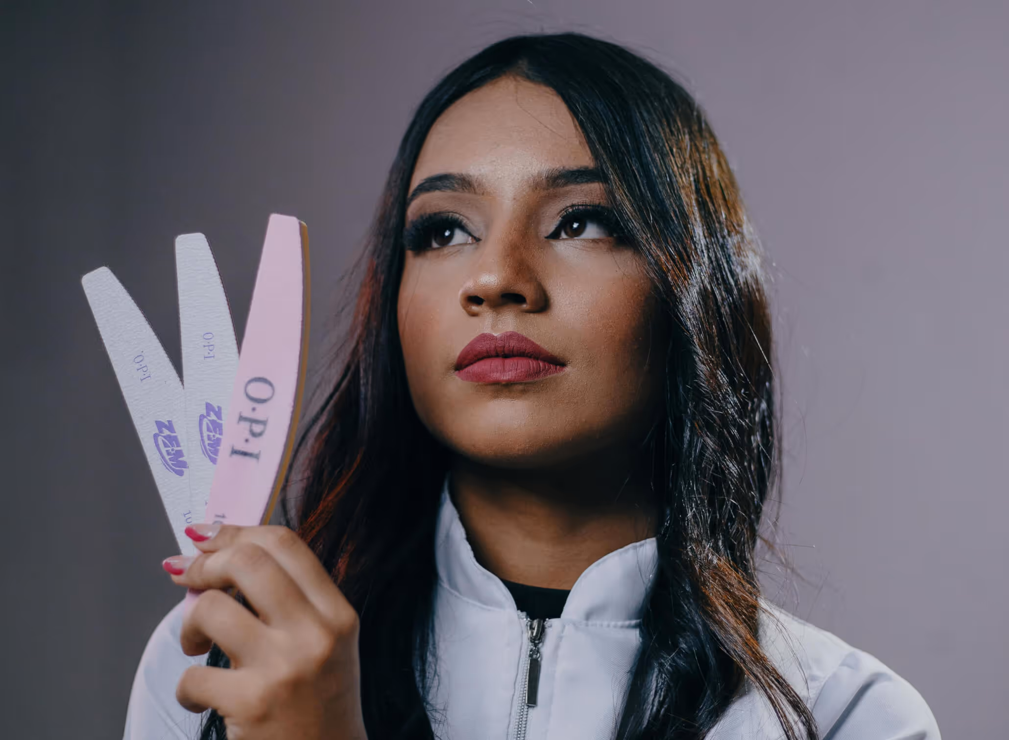 Woman with long dark hair and bold lipstick holding three nail files labeled OPI.