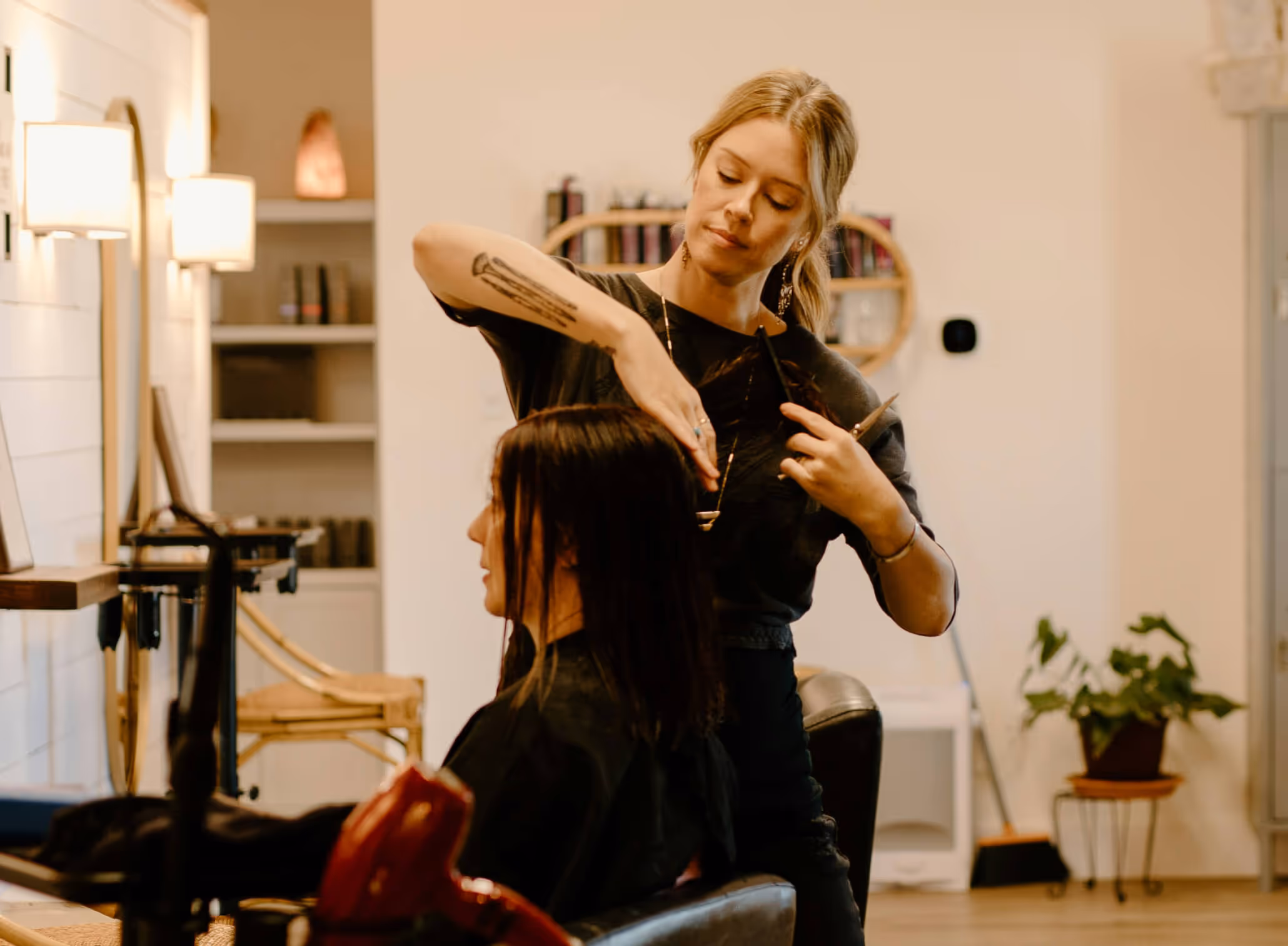 Hairdresser cutting a seated woman's wet hair in a cozy salon.