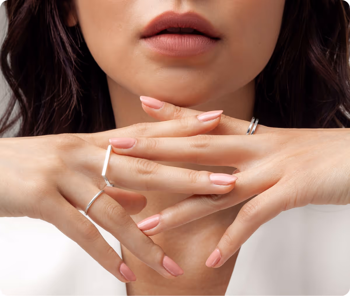 Close-up of a woman's lips and hands with light pink manicured nails and silver rings on fingers.