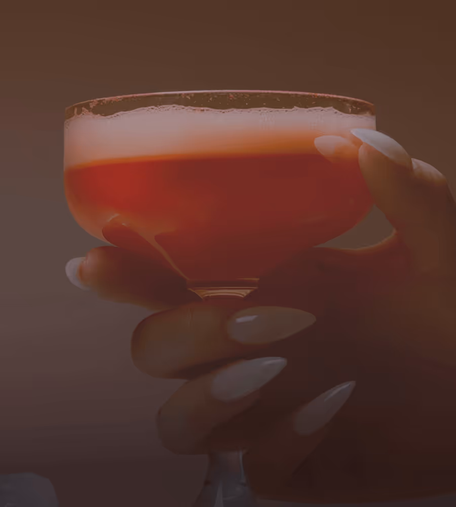 Hand with long, manicured nails holding a glass of red cocktail with a salted rim.
