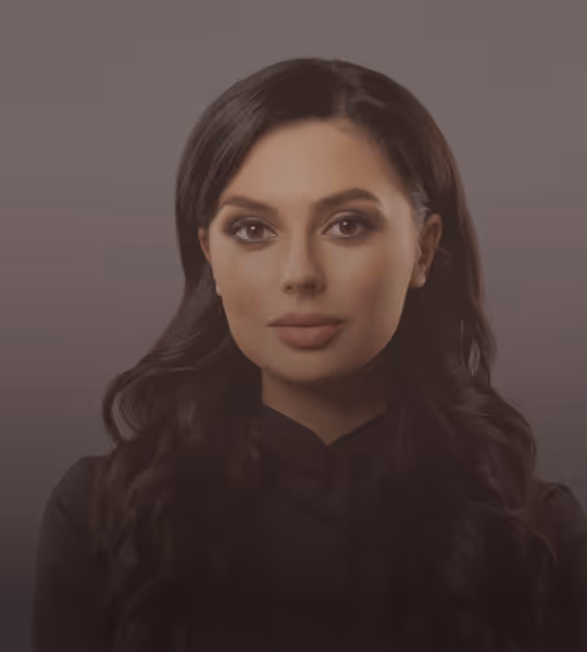 Portrait of a woman with long dark hair, wearing a black top against a plain gray background.