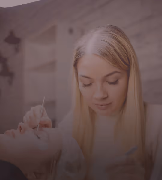 Beauty technician applying eyelash extensions to a client lying down.