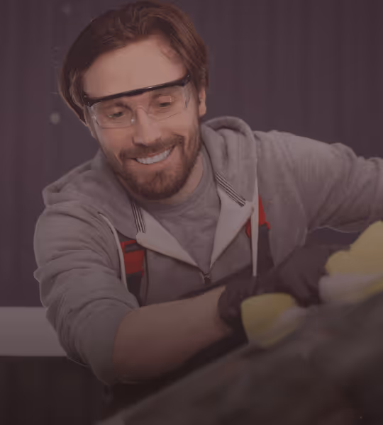 Smiling man wearing protective glasses and gloves polishing a surface with a yellow cloth.