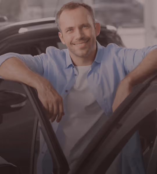 Smiling man standing beside an open car door in a bright indoor setting.