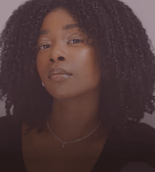 Portrait of a woman with natural curly hair, wearing subtle makeup and a delicate necklace.