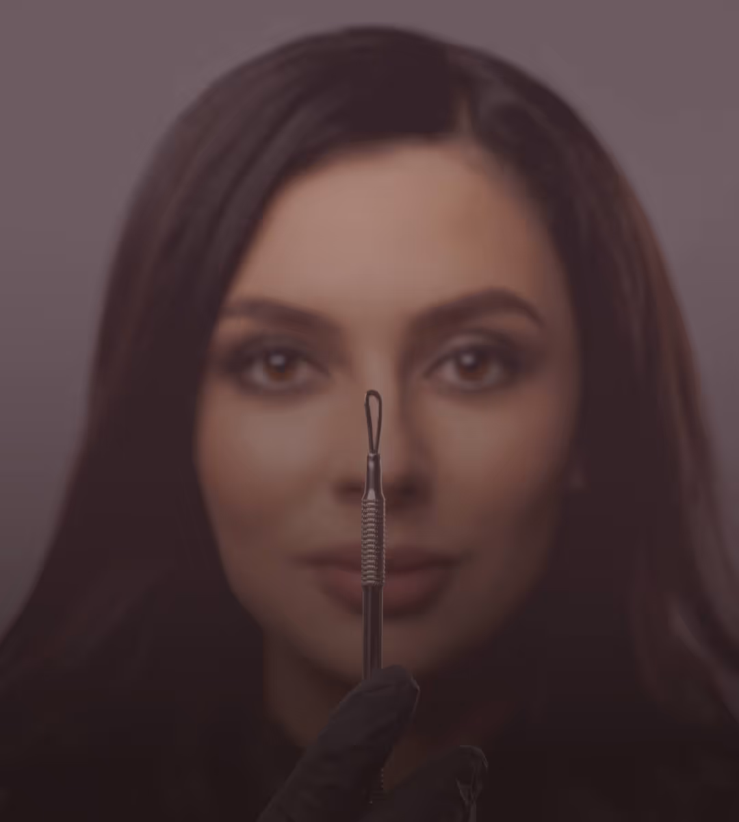 Close-up of a woman with dark hair holding a metal extraction tool in front of her face, wearing a black glove.