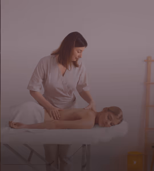 A woman receives a back massage from a massage therapist in a calm, minimalist room.