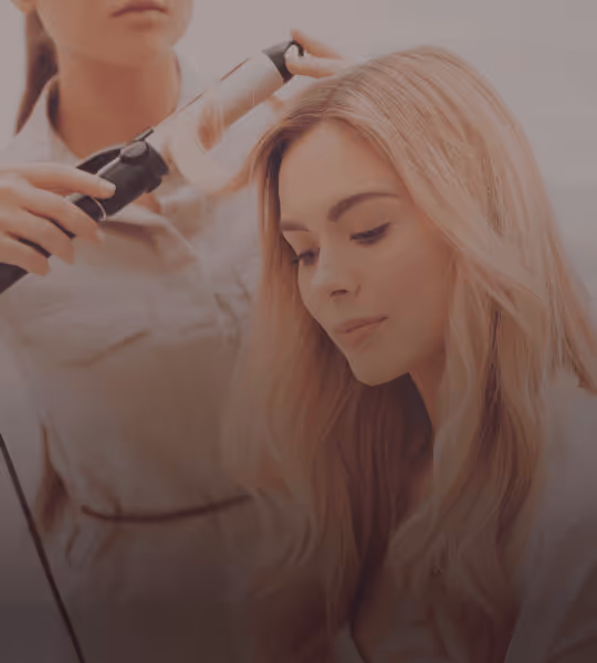 Hairdresser curling long blonde hair of a seated woman in a salon.