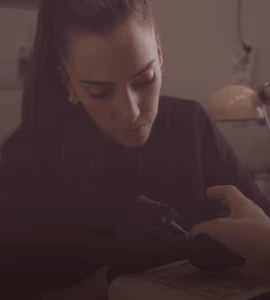 A woman focused on giving a tattoo on someone's arm in a dimly lit room.