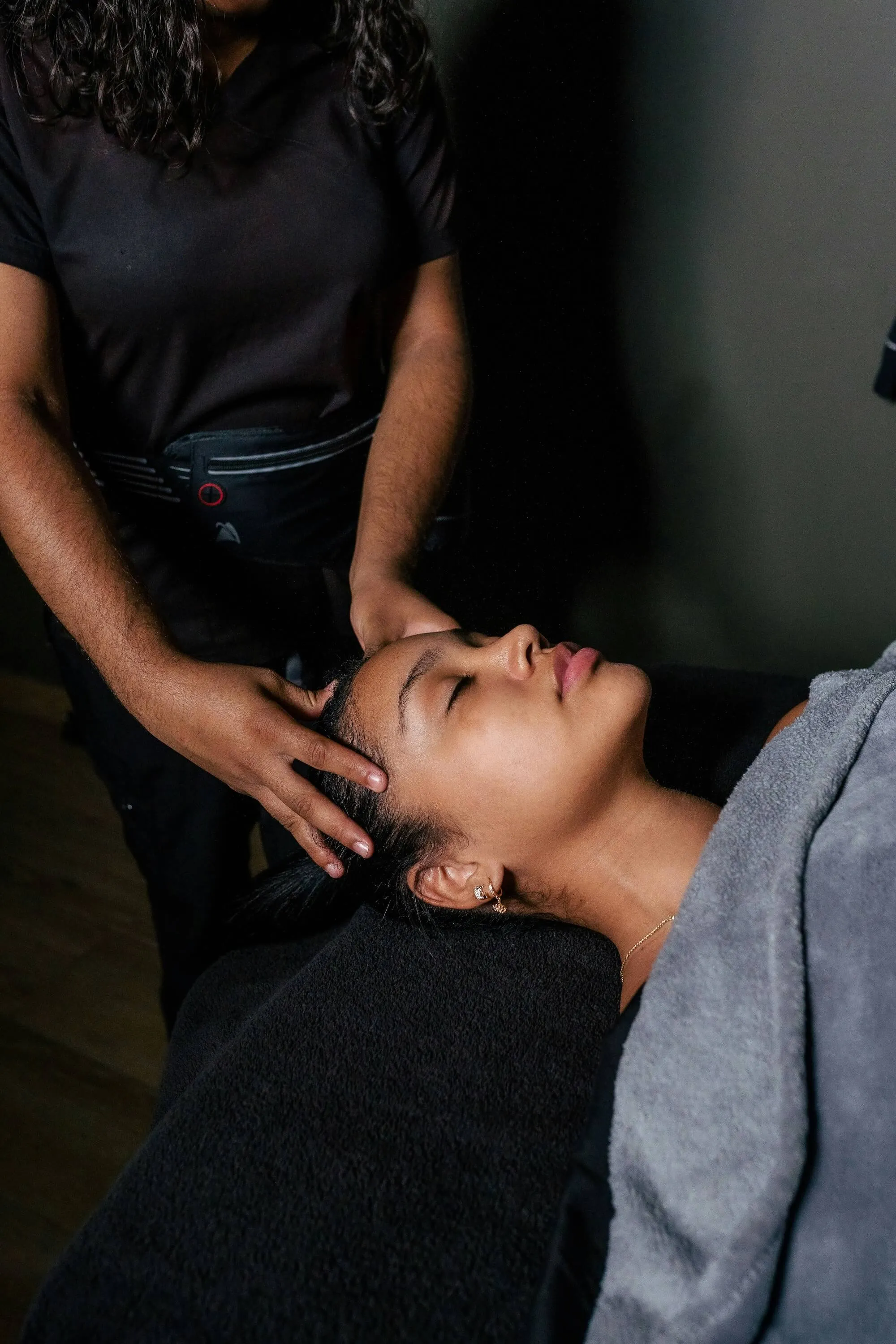 Person receiving a calm head massage while lying covered with a gray towel.