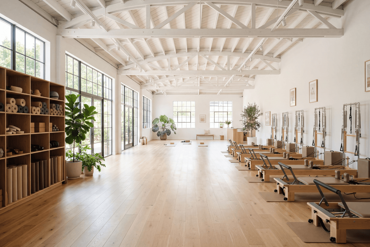 Spacious hybrid pilates studio with reformer machines on one side and mat props shelving on the other, open floor space in the center