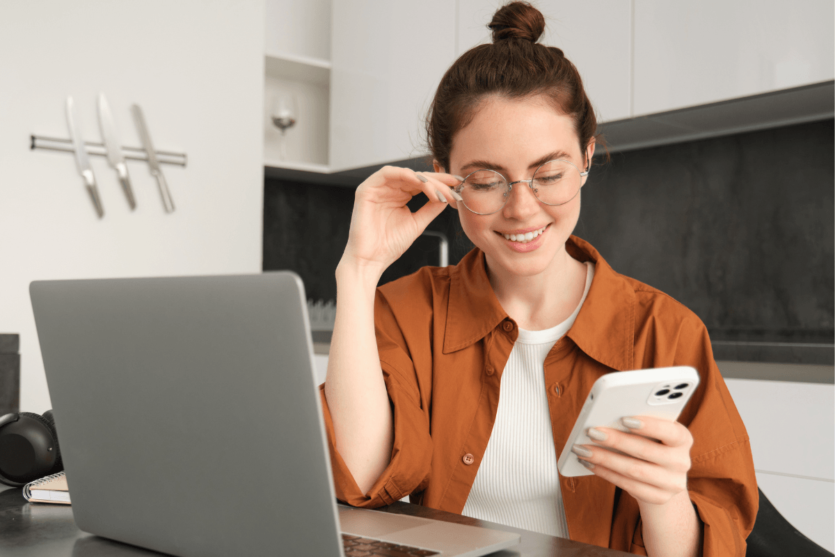 Woman at home using her phone and laptop to book a beauty appointment online.