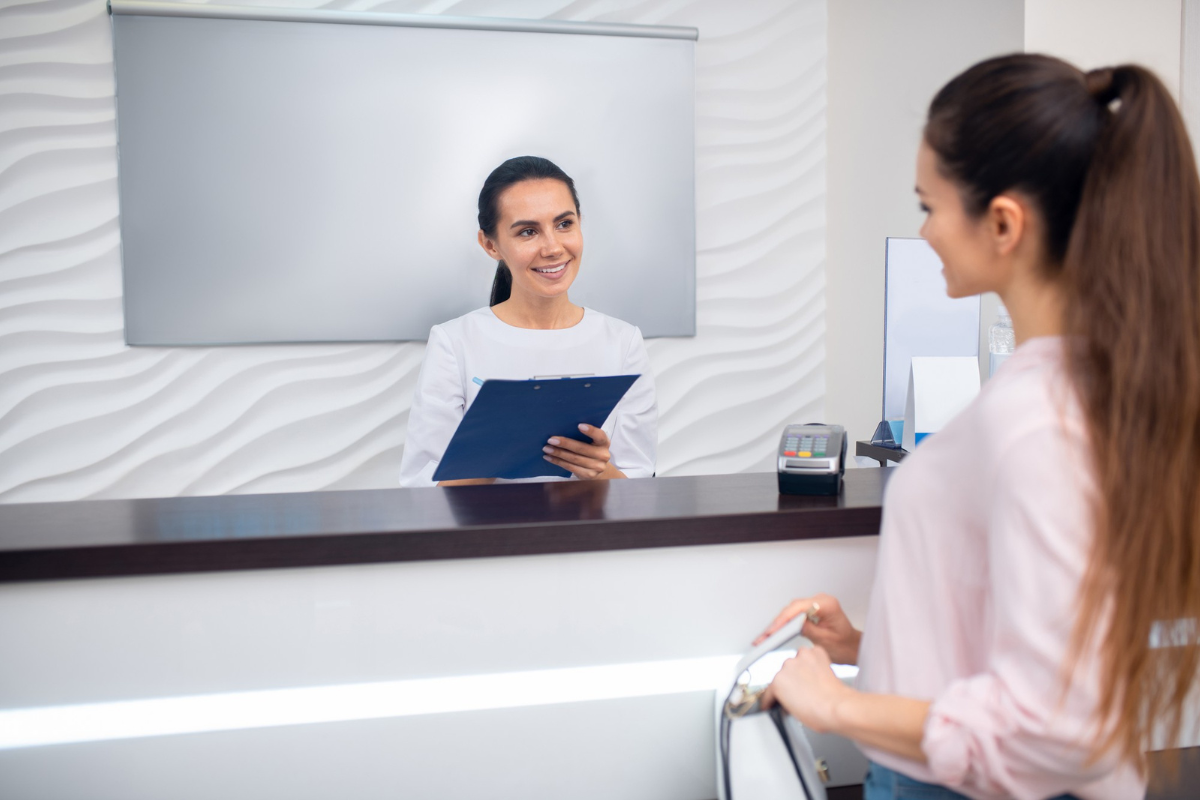 Client speaking with a beauty professional at the salon reception desk beside a card payment terminal.