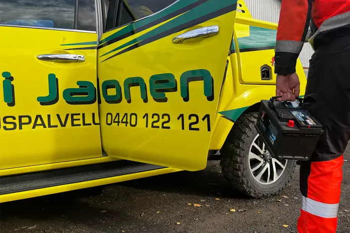 Tiepalvelun työntekijä kantaa uutta auton akkua Oili Jalosen huoltoauton vierellä.