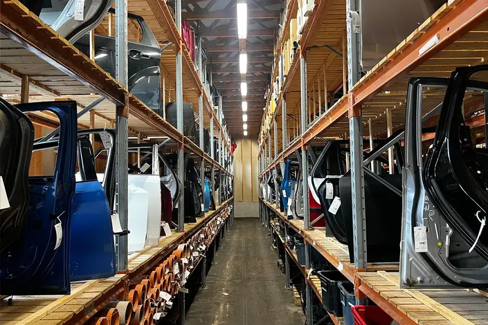 Järjestelmällinen varaosavarasto, jossa on hyllyittäin auton ovia ja muita purkuosia valmiina toimitukseen.