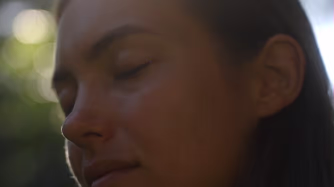 A close-up of a woman with her eyes closed in soft light.