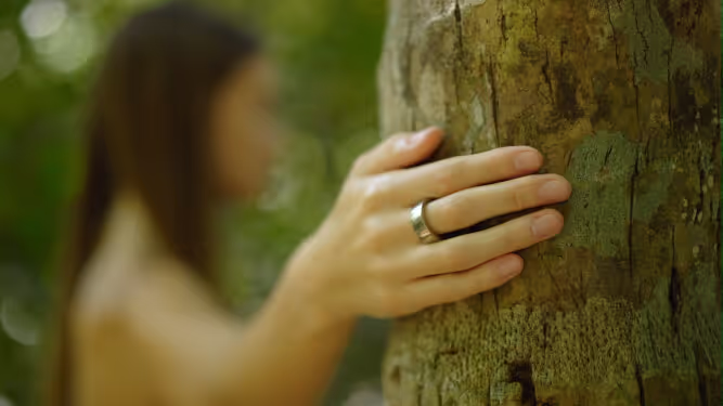 A woman resting her hand, wearing the Pulse Ring, on a tree trunk.