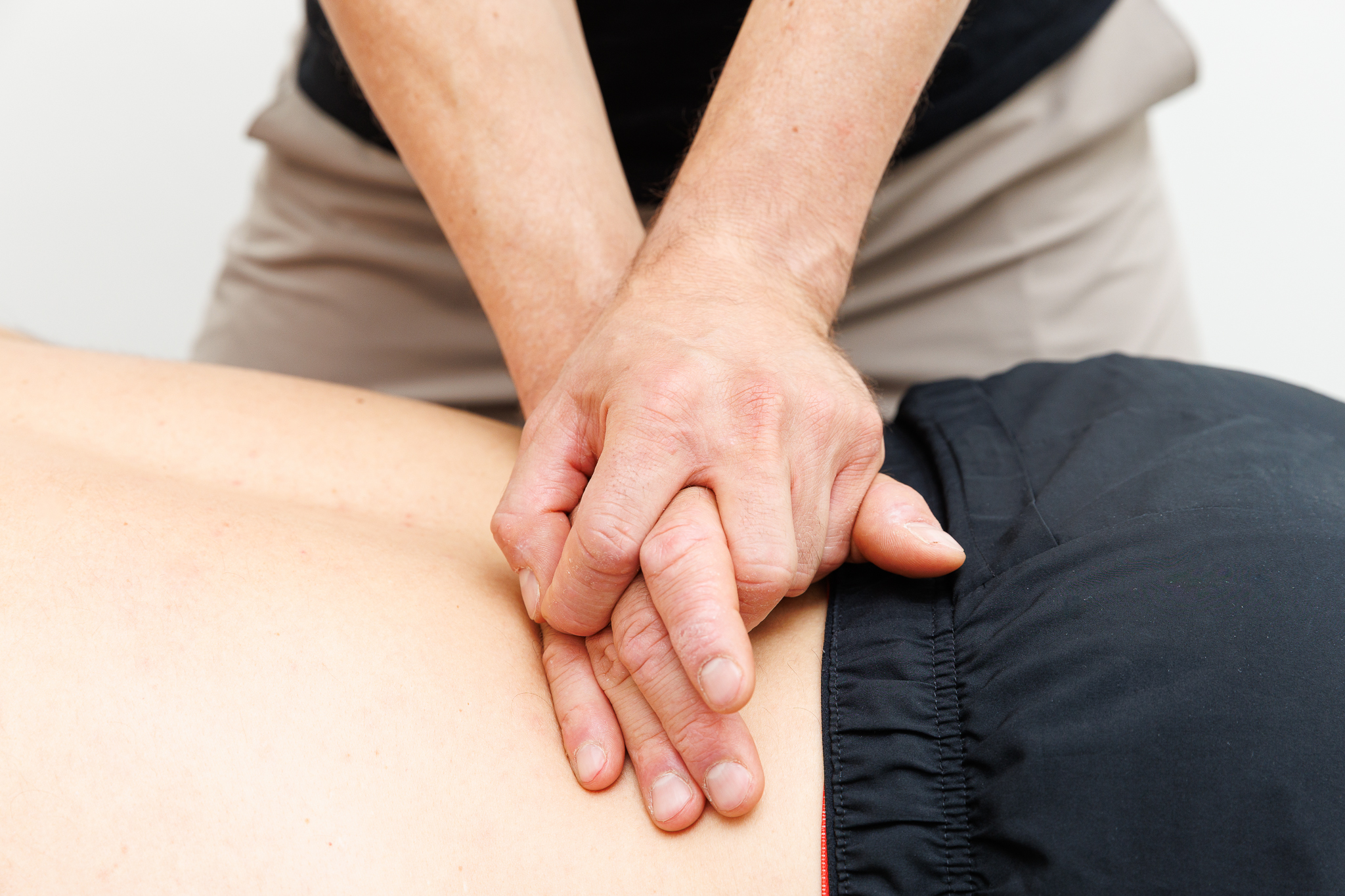 Mains d’un praticien exerçant une pression sur le bas du dos d’une personne couchée, lors d’une séance de massage ou de kinésithérapie.