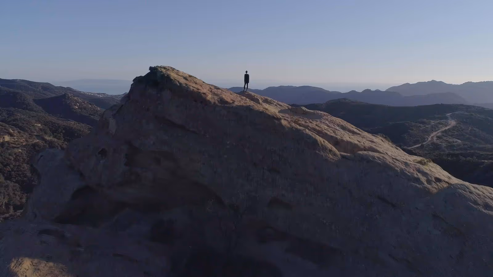 Narcissa Wright (she / her) stands in silhouette, alone on top of a mountain.