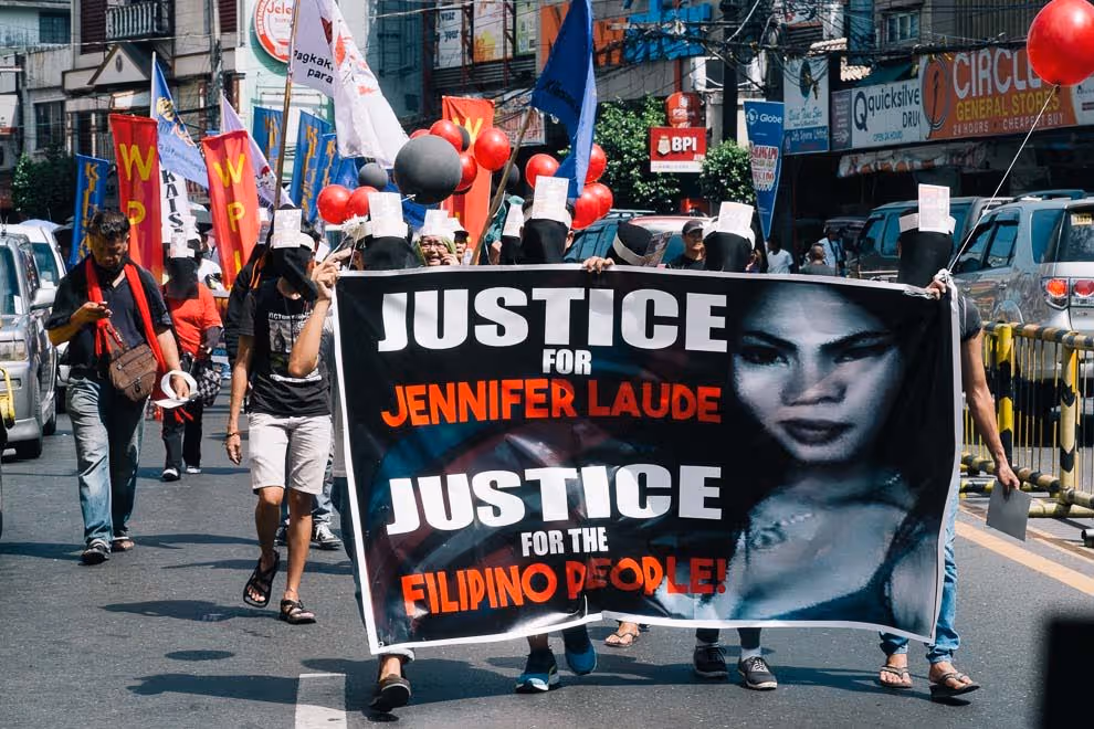 Protestors carry a large banner with a black background, white and red text that reads "Justice for Jennifer Laude, Justice for Filipino People
