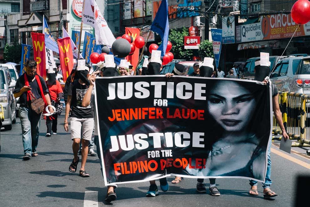 Protestors carry a large banner with a black background, white and red text that reads "Justice for Jennifer Laude, Justice for Filipino People