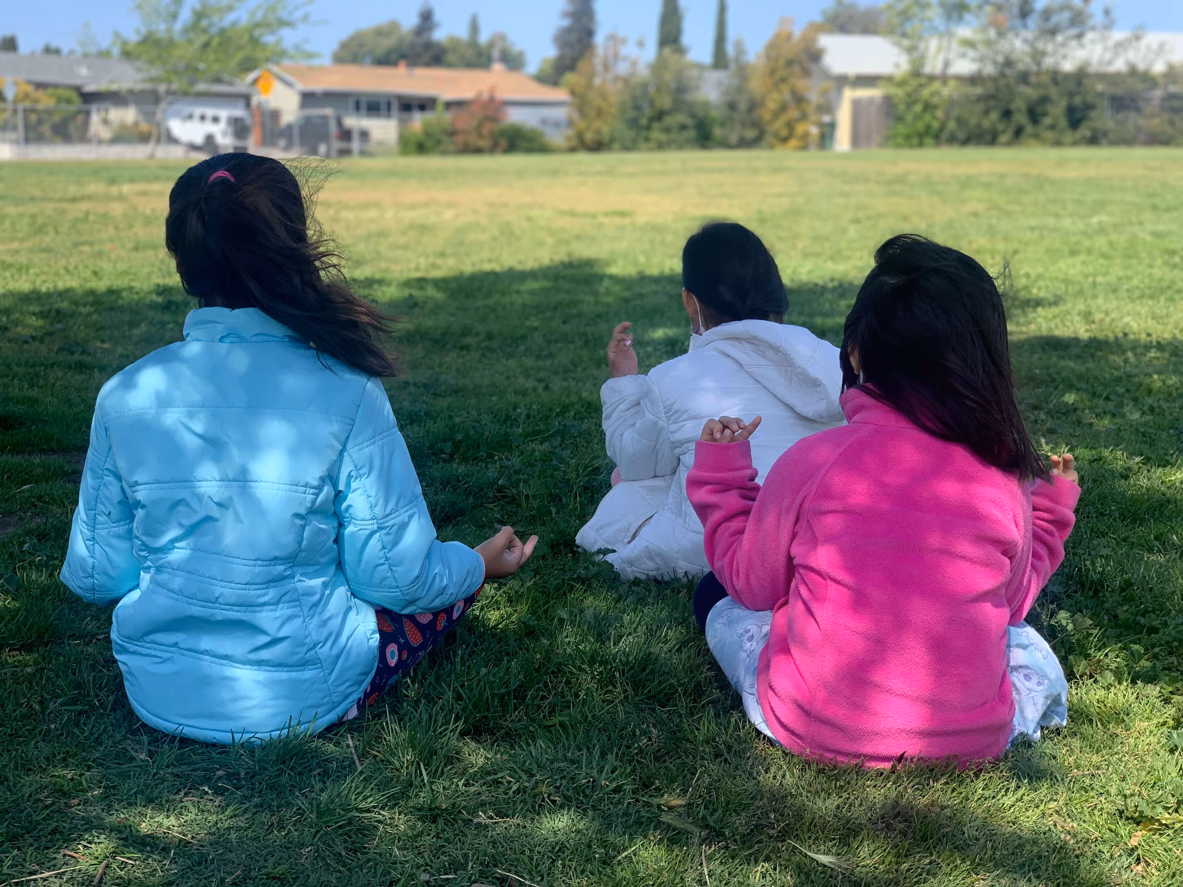 Three people in colorful jackets sitting on grass, viewed from behind