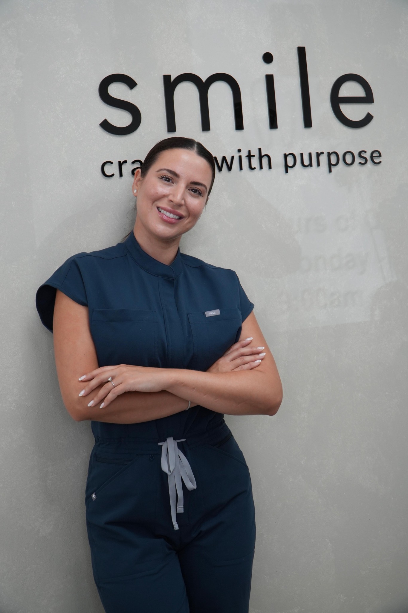 Dr. Emmy Estenoz in blue scrubs in front of the smile sign at Coconut Creek Cosmetic & Implant Dentistry