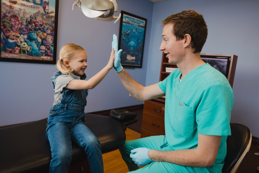 Young child smiles and high-fives a pediatric dentist during a dental checkup at Just 4 kiDDS Pediatric Dentistry, showcasing a kid-friendly dental environment.
