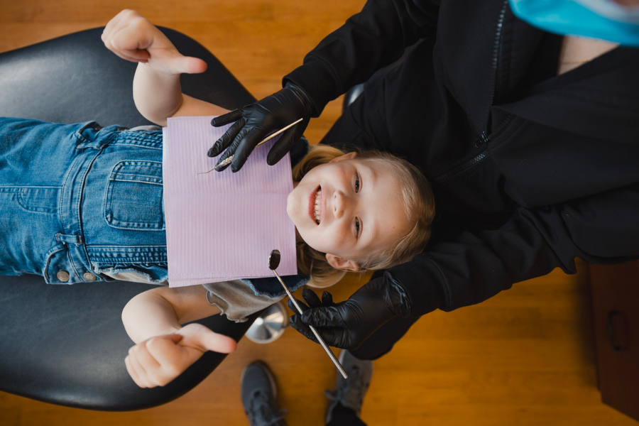 Young child smiling and giving two thumbs up while lying in a dental chair during a pediatric exam at Just 4 kiDDS Dentistry, showing a relaxed and positive experience.