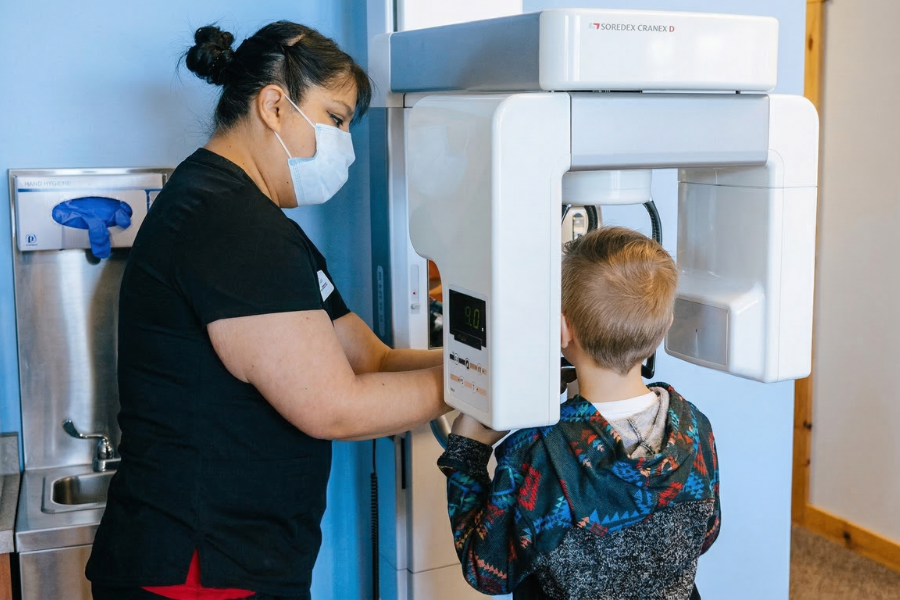 Pediatric dental assistant helping a child stand in a panoramic dental X-ray machine during a routine visit at a pediatric dentist in Idaho Falls.