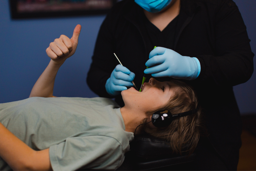 Young patient wearing headphones and giving a thumbs-up during a comfortable pediatric dental exam and routine cleaning appointment.