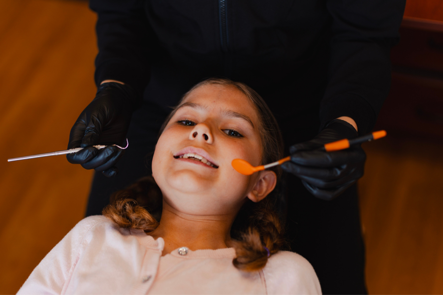 Young girl smiling during a pediatric dental checkup while a dentist prepares for a routine teeth cleaning and oral examination.