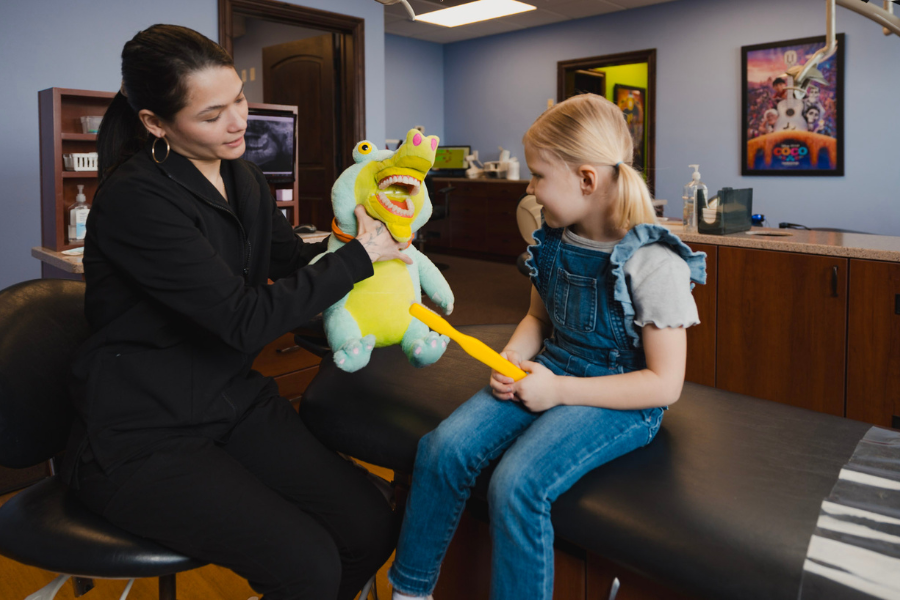 Pediatric dental professional teaching a young girl about brushing with a stuffed animal during a dental visit.