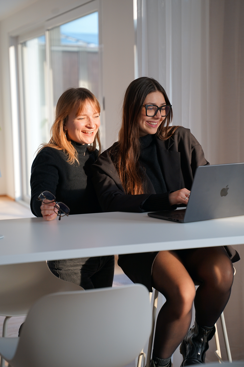 Smiling woman typing on a laptop at a white standing desk in a modern room.