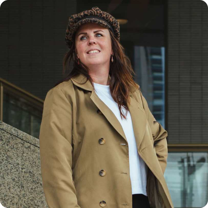 Lindsey van Studio Maker in een camel trenchcoat en luipaardpet, lachend omhoog kijkend