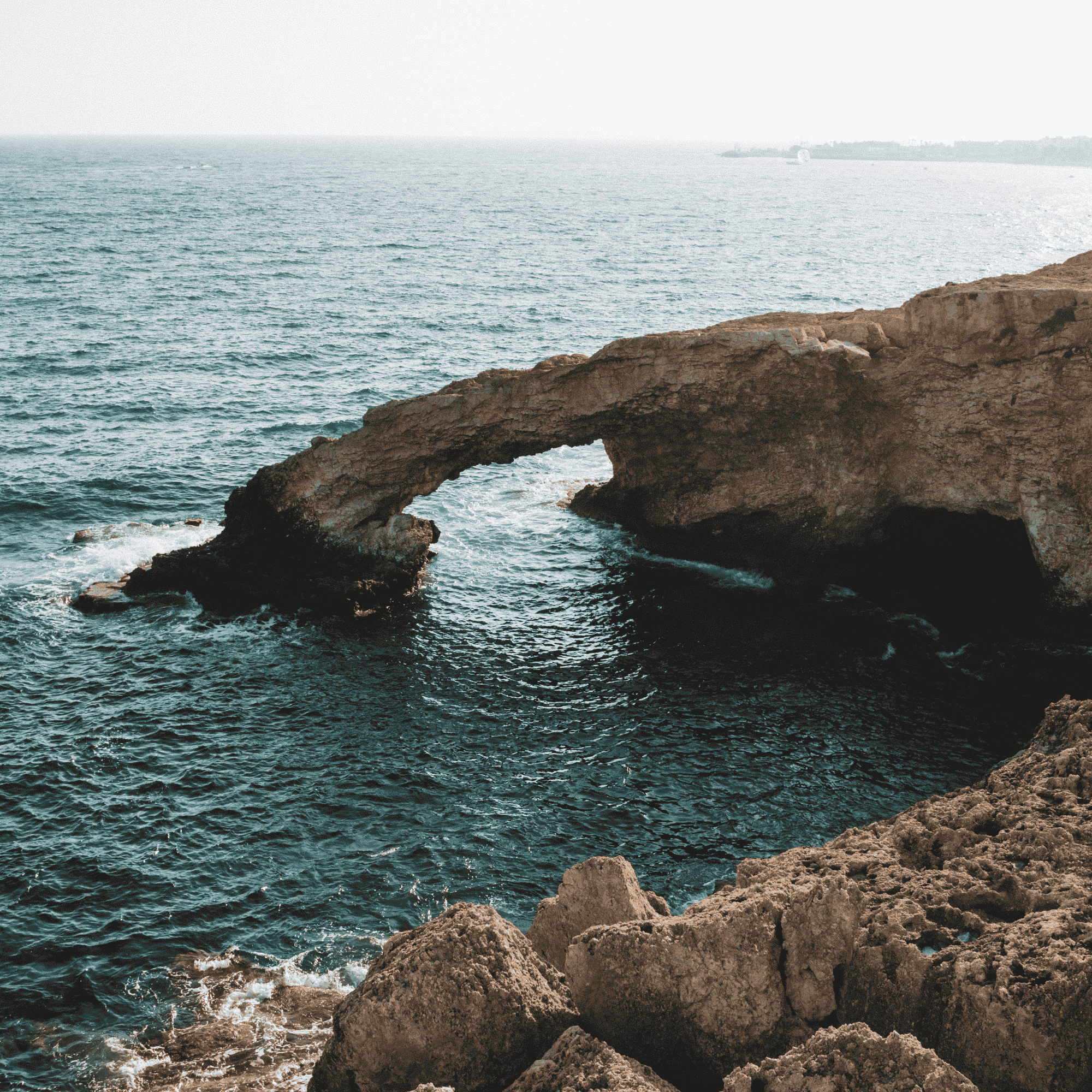Natural rock arch bridge over clear blue sea in Cyprus, symbolizing the strong and solid foundation of economic substance for a Cyprus company.