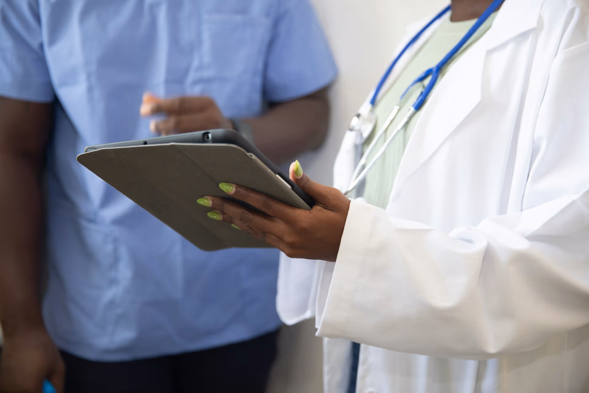 A healthcare professional in a white coat holding a clipboard, standing beside another individual in medical scrubs. This image symbolizes collaboration and precision.