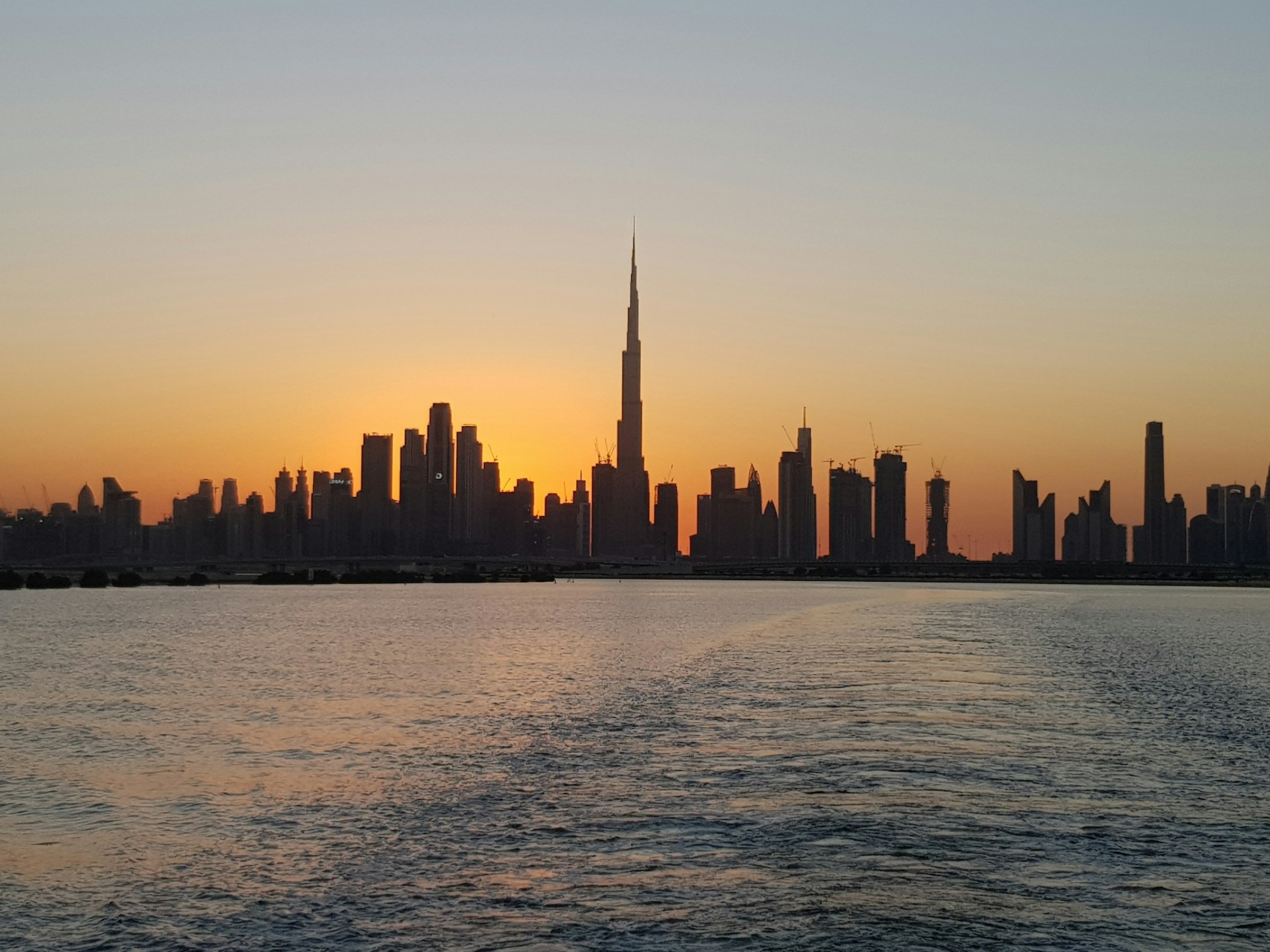 Dubai skyline at sunset with the Burj Khalifa and surrounding skyscrapers reflecting on the water, linking to the blog post 'Why is Dubai the Hub for Substantial Investments?