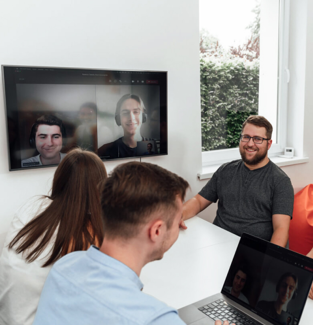 Software development team conducting hybrid meeting with remote colleagues joining via video call on wall-mounted screen