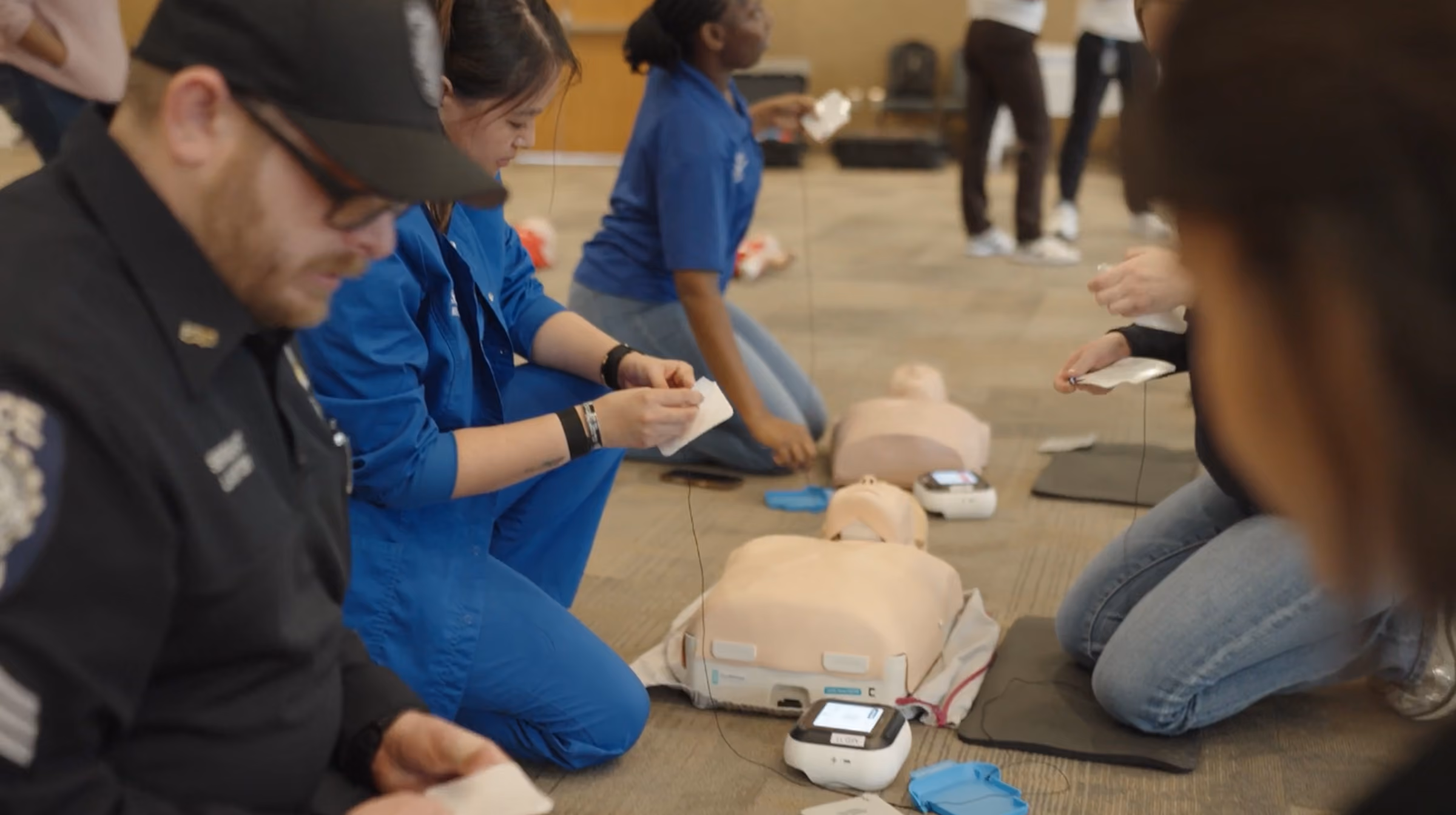 People in a CPR training session kneeling by manikins and preparing AED pads.