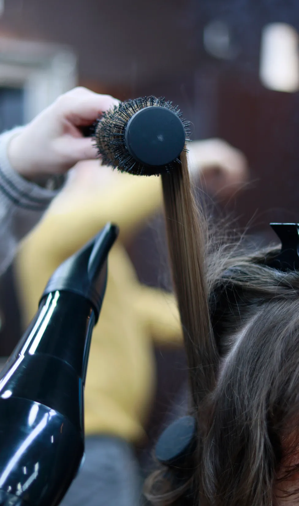 Hairstylist using round brush and hairdryer to style hair